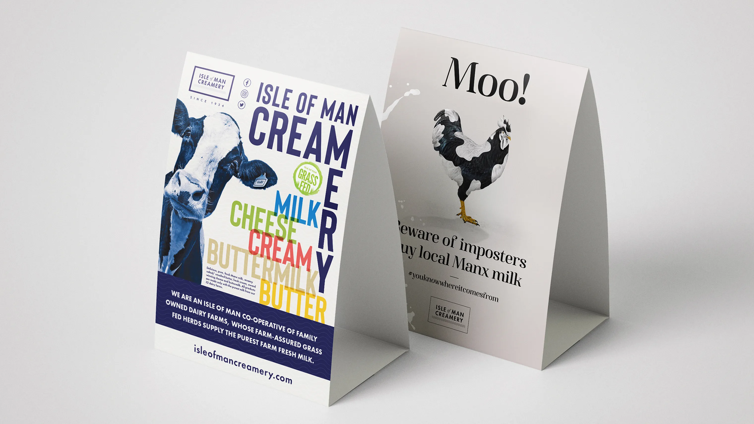 Two-sided table tent card for Isle of Man Creamery. The front panel features bold colorful text listing products: Milk, Cheese, Cream, Buttermilk, Butter. The back panel shows a rooster with the text "Moo! Beware of imposters, Buy local Manx milk" and the Isle of Man Creamery logo.